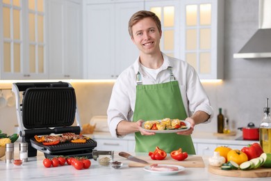 Photo of Man cooking meat and vegetables on electric grill in kitchen