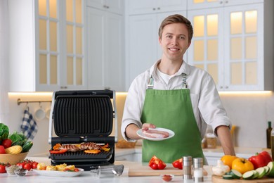 Photo of Man cooking meat and vegetables on electric grill in kitchen