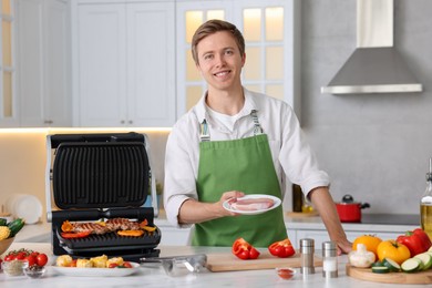Photo of Man cooking meat and vegetables on electric grill in kitchen