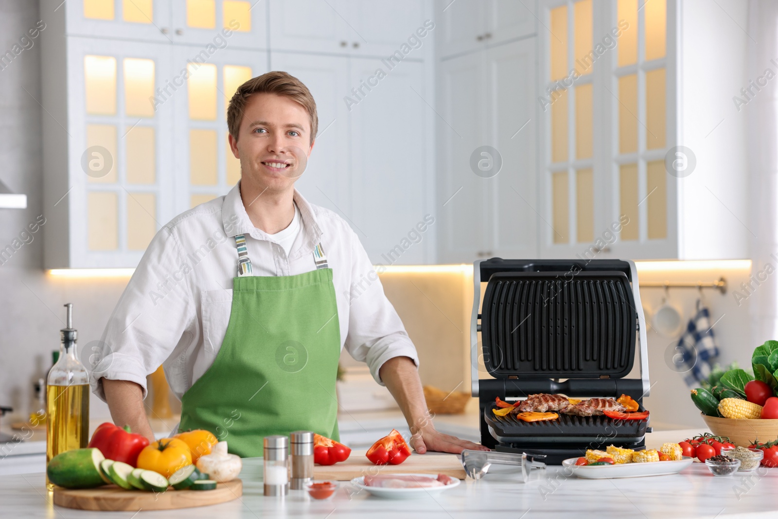 Photo of Man cooking meat and vegetables on electric grill in kitchen