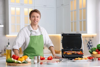 Photo of Man cooking meat and vegetables on electric grill in kitchen