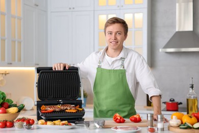 Photo of Man cooking meat and vegetables on electric grill in kitchen