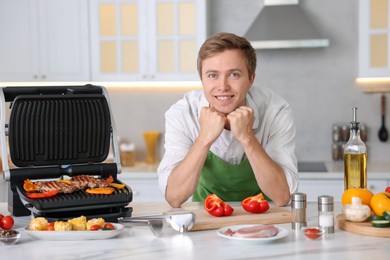 Photo of Man cooking meat and vegetables on electric grill in kitchen