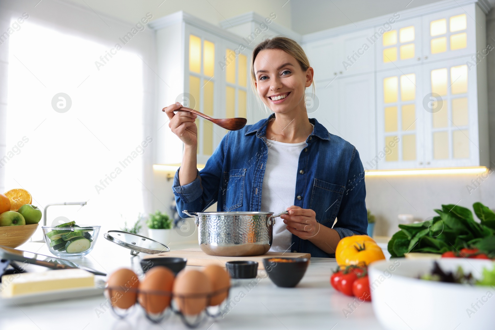 Photo of Smiling woman tasting meal after cooking at table in kitchen