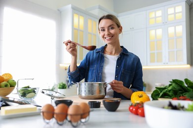 Photo of Smiling woman tasting meal after cooking at table in kitchen