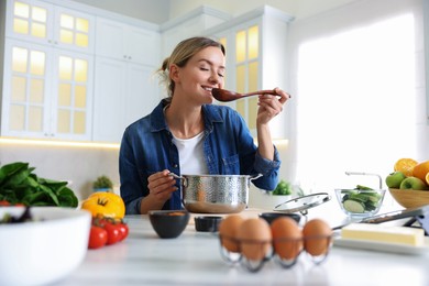 Photo of Smiling woman tasting meal after cooking at table in kitchen