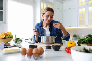 Photo of Smiling woman sniffing meal after cooking at table in kitchen