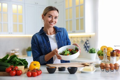 Photo of Smiling woman showing freshly cooked salad at table in kitchen