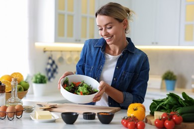 Photo of Smiling woman showing freshly cooked salad at table in kitchen