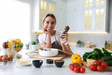 Photo of Cooking process. Portrait of smiling woman with black pepper at table in kitchen