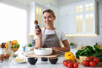 Photo of Cooking process. Portrait of smiling woman with black pepper at table in kitchen