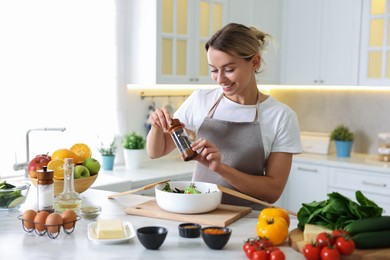 Photo of Cooking process. Smiling woman seasoning salad at table in kitchen