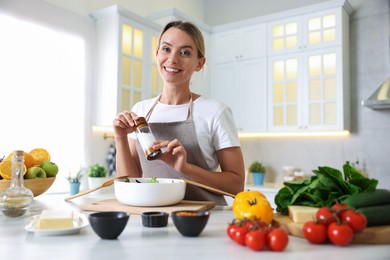 Photo of Cooking process. Smiling woman seasoning salad at table in kitchen