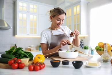 Photo of Cooking process. Smiling woman seasoning salad at table in kitchen