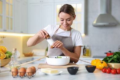 Photo of Cooking process. Smiling woman seasoning salad at table in kitchen