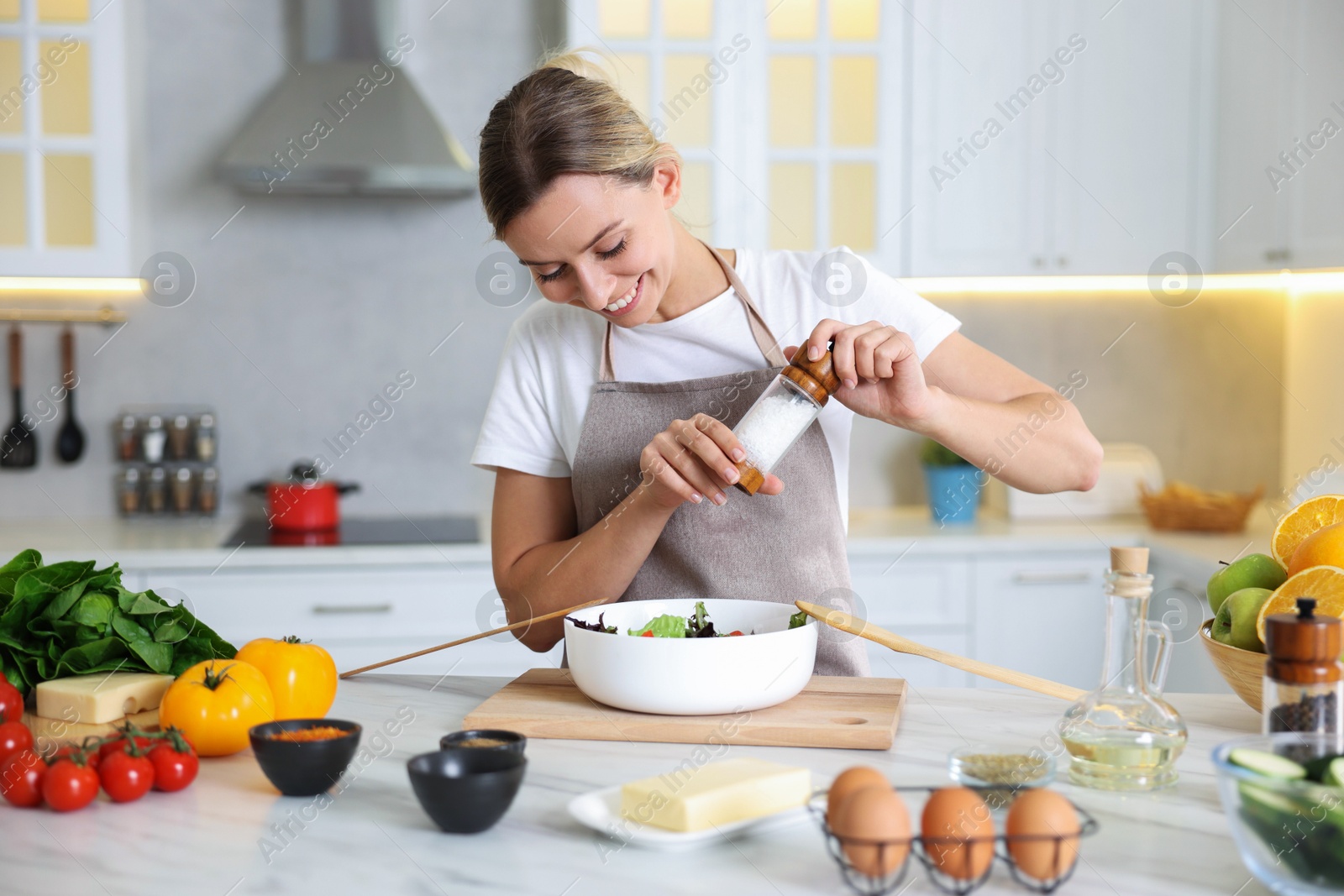 Photo of Cooking process. Smiling woman seasoning salad at table in kitchen
