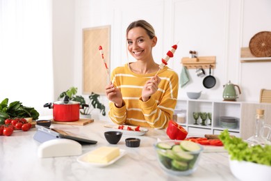 Photo of Smiling woman with tasty skewers after cooking at table in kitchen