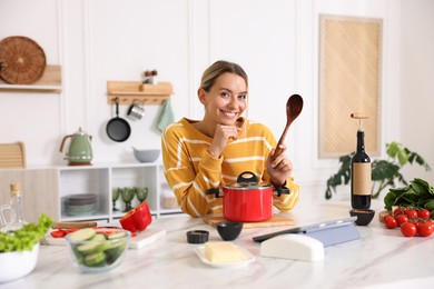 Photo of Portrait of smiling woman with spoon cooking at table in kitchen