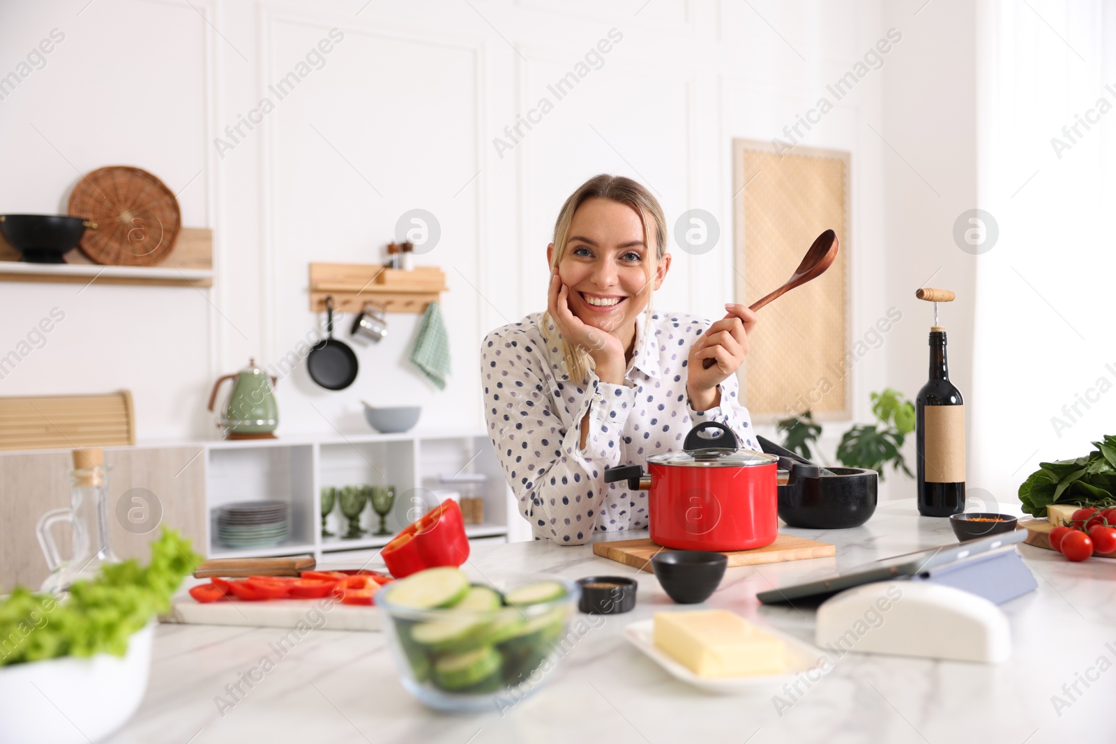 Photo of Portrait of smiling woman with spoon cooking at table in kitchen