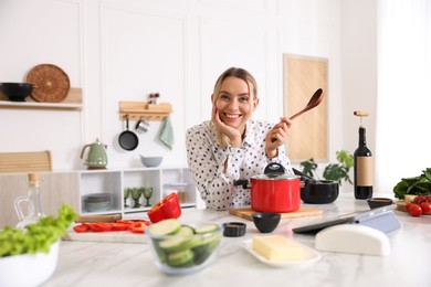 Photo of Portrait of smiling woman with spoon cooking at table in kitchen