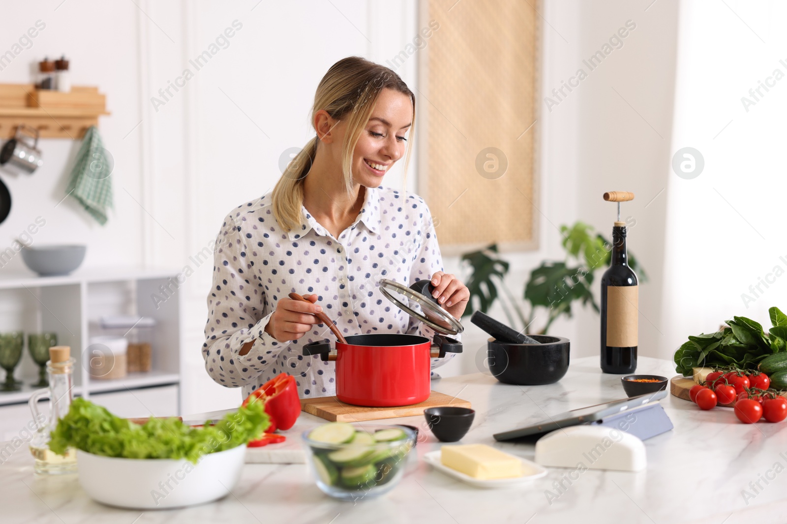 Photo of Smiling woman looking at recipe on tablet while cooking at table in kitchen