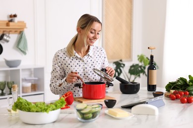 Photo of Smiling woman looking at recipe on tablet while cooking at table in kitchen