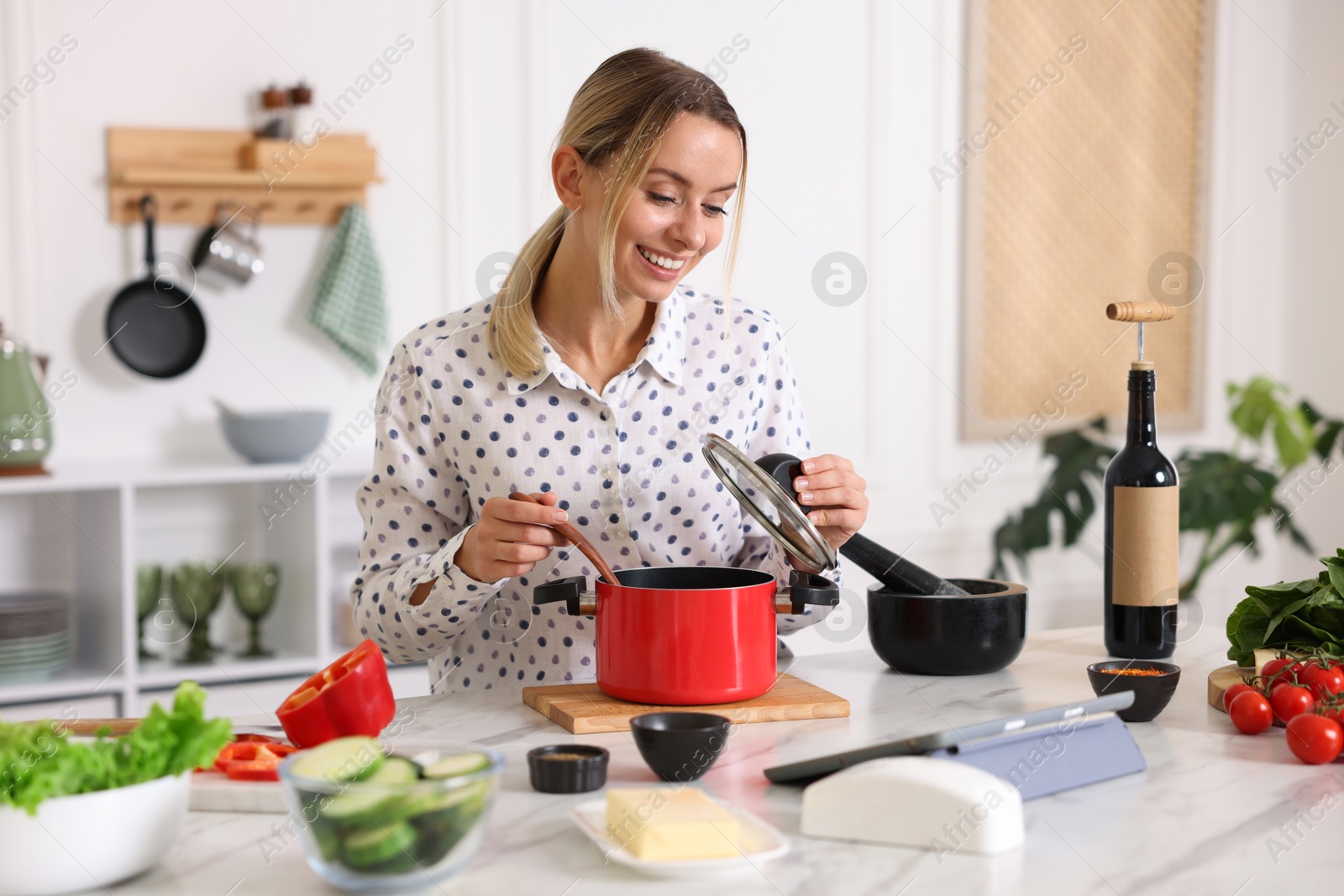 Photo of Smiling woman looking at recipe on tablet while cooking at table in kitchen