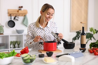 Photo of Smiling woman looking at recipe on tablet while cooking at table in kitchen
