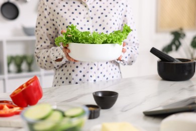 Photo of Cooking process. Woman with bowl of lettuce at marble table indoors, closeup