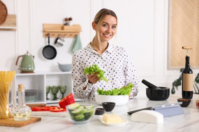 Photo of Cooking process. Smiling woman with bowl of lettuce at table in kitchen