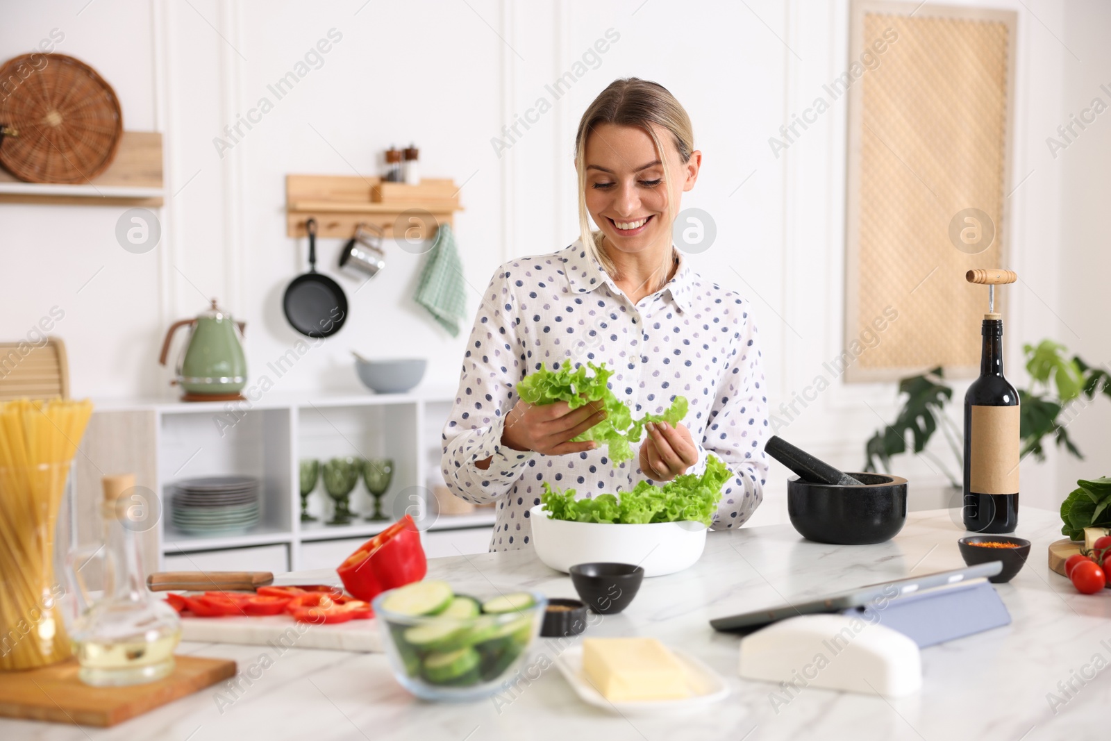 Photo of Cooking process. Smiling woman with bowl of lettuce at table in kitchen