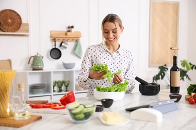 Photo of Cooking process. Smiling woman with bowl of lettuce at table in kitchen
