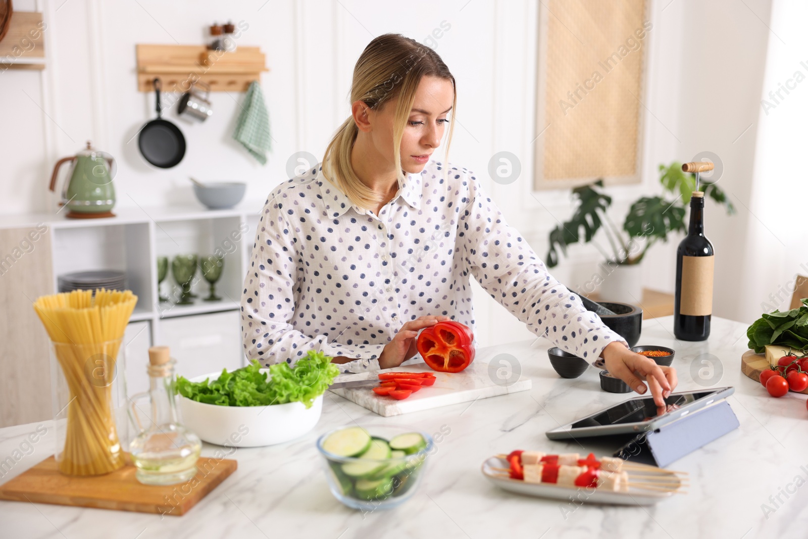 Photo of Beautiful woman looking at recipe on tablet while cooking at table in kitchen