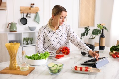 Photo of Beautiful woman looking at recipe on tablet while cooking at table in kitchen