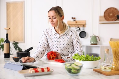 Photo of Beautiful woman looking at recipe on tablet while cooking at table in kitchen