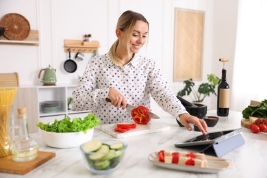 Photo of Smiling woman looking at recipe on tablet while cooking at table in kitchen