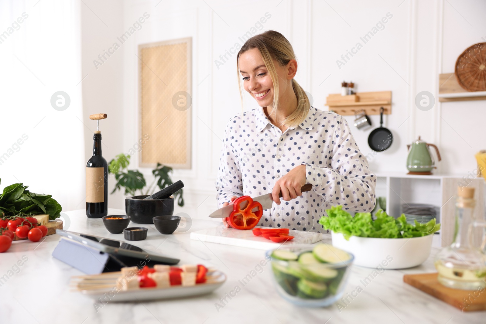 Photo of Smiling woman looking at recipe on tablet while cooking at table in kitchen