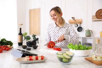 Photo of Smiling woman looking at recipe on tablet while cooking at table in kitchen