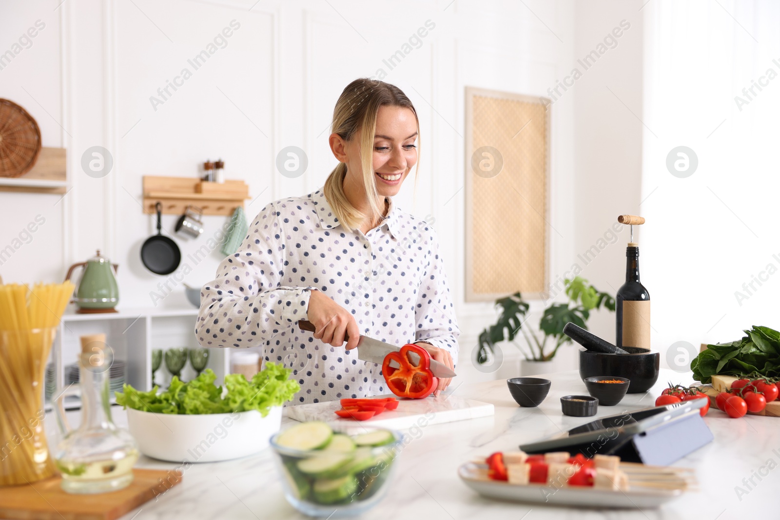 Photo of Smiling woman looking at recipe on tablet while cooking at table in kitchen