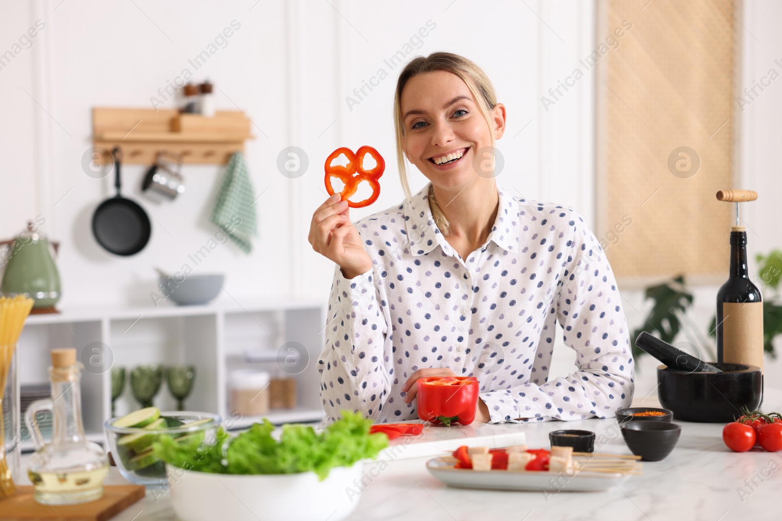 Photo of Smiling woman showing slice of bell pepper while cooking at table in kitchen