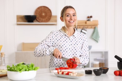 Photo of Cooking process. Smiling woman cutting bell pepper at table in kitchen