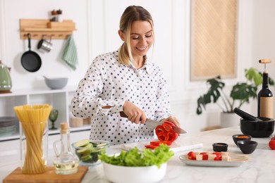 Photo of Cooking process. Smiling woman cutting bell pepper at table in kitchen