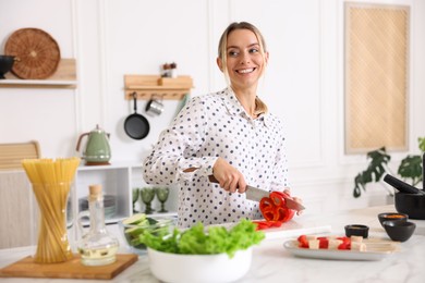 Photo of Cooking process. Smiling woman cutting bell pepper at table in kitchen