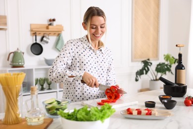 Photo of Cooking process. Smiling woman cutting bell pepper at table in kitchen