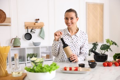 Photo of Smiling woman opening bottle of wine while cooking at table in kitchen