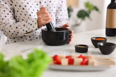 Photo of Woman with mortar cooking at table indoors, closeup