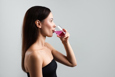 Photo of Young woman rinsing mouth with mouthwash on grey background, space for text. Oral hygiene