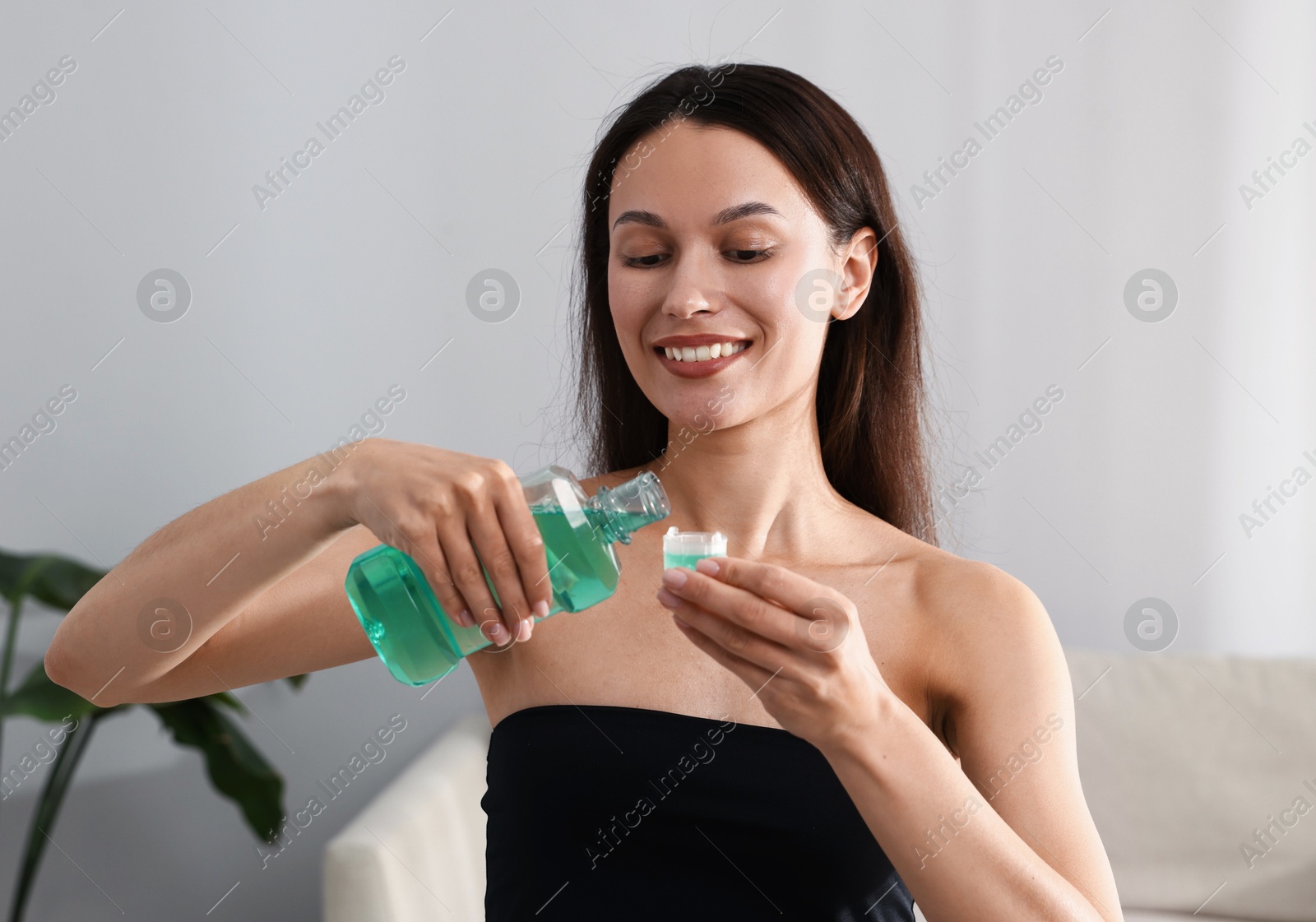 Photo of Smiling young woman pouring mouthwash into cap at home. Oral hygiene