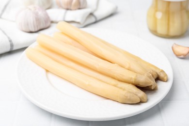 Photo of Pickled asparagus and garlic on white tiled table, closeup
