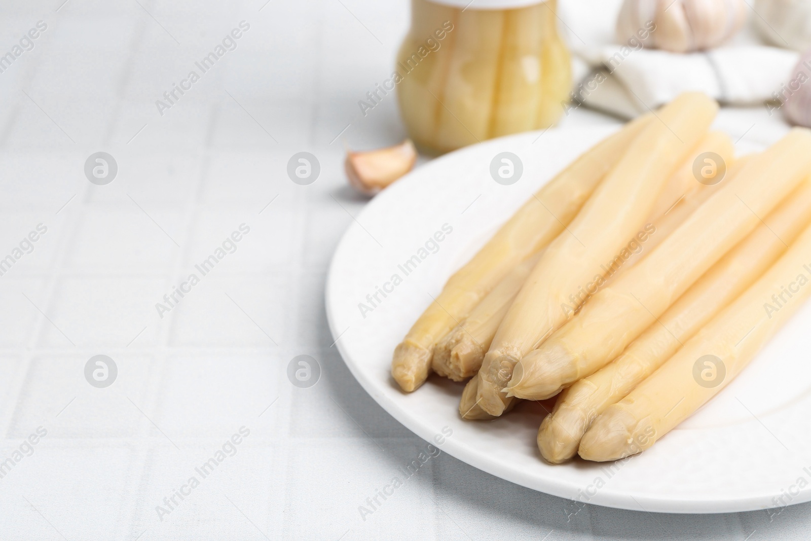 Photo of Pickled asparagus and garlic on white tiled table, closeup. Space for text